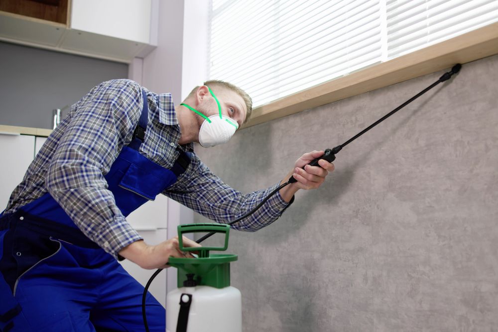 A man in overalls applies spray to a wall, showcasing pest control services in Floor, Miami, FL.